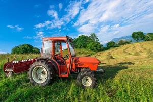 tractor rojo en un prado de montaña con fardos de heno hechos a mano foto