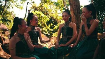 un groupe de femmes asiatiques riant et assises ensemble dans une robe verte tout en rencontrant leur amie dans la forêt