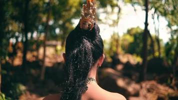 A Balinese dancer sitting on a big rock with a lot of trees in the background while enjoying the view inside the jungle video