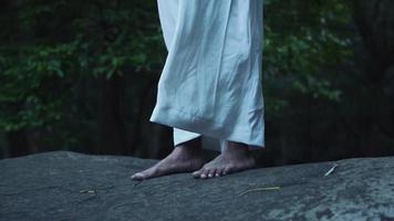 un arabo uomo in piedi su il grigio roccia nel il foresta con bianca Abiti video