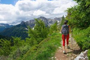 chica con mochila y bastones durante un trekking alpino sola foto