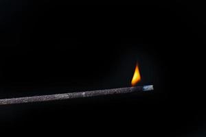 Eastern incense stick with burning flame on black background photo