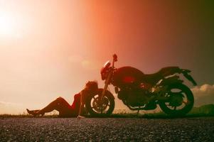 chica descansando al sol sol apoyada contra el volante de su motocicleta foto