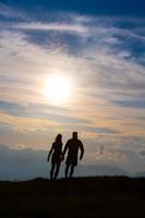 pareja en silueta tomados de la mano caminando hacia nubes coloridas al atardecer en las montañas