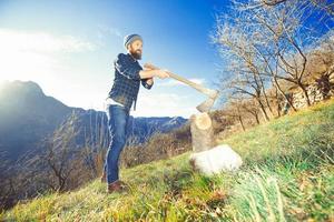 Young man with lumberjack beard cuts wood photo