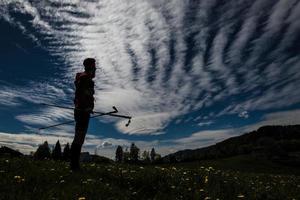 A trekker man with sticks at dusk stops watching the landscape photo