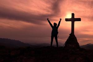 Cross at the top of the mountain with a mountaineer who raises his hands photo