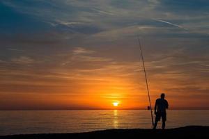 pescador en el mar durante la puesta de sol foto