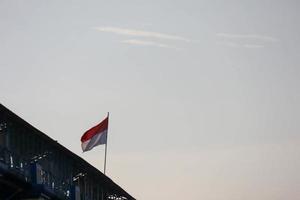 The Indonesian red and white flagpole flutters against a cloudy sky background photo