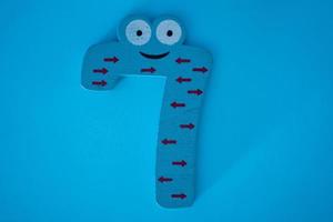 Cute and colorful wooden number 7 with eyes on a blue background. photo
