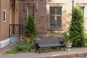 Wooden bench on the background of a brick house with flowers and trees. photo