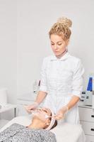 Cosmetologist applying cosmetic cream mask on female face for rejuvenation procedure in beauty salon photo