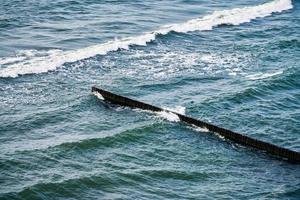 antiguos rompeolas de madera largos que se extienden hasta aguas profundas del mar azul, olas espumosas, paisaje marino foto