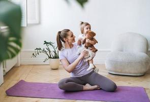 mujer joven en forma mamá con niña haciendo fitness en la alfombra en casa foto