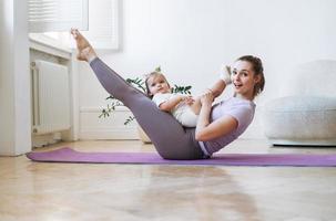 mujer joven en forma mamá con niña haciendo fitness en la alfombra en casa foto