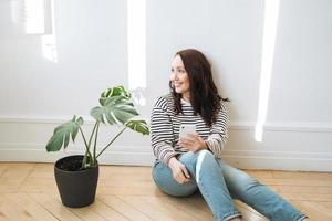 mujer morena sonriente con ropa informal usando un teléfono móvil en casa foto