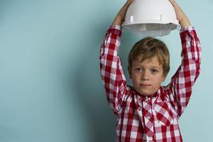 A cute boy in a plaid shirt holds a construction helmet over his head, A portrait of a small builder photo