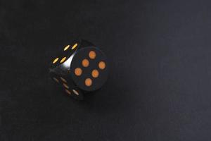 A black dice standing in balance on an edge and showing 6 on a black table photo