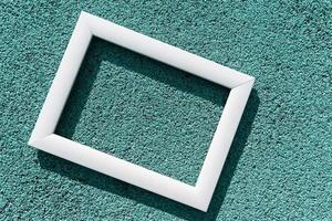 An empty white frame on a turquoise textured background, with a copy space. Minimal concept photo