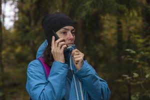 A tourist girl is talking on the phone in the forest, a tourist got lost in the forest. Call for help photo