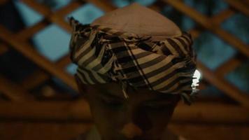 un' musulmano ragazzo seduta nel davanti di il bambù modello parete dentro il tradizionale bambù Casa a notte video