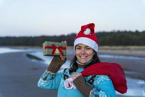 Happy young woman in a Christmas cap takes Christmas gifts out of the bag photo