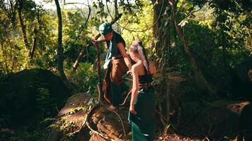 An Asian couple in green clothes walking to the top of a big rock in the mountain near the forest while visiting the village video