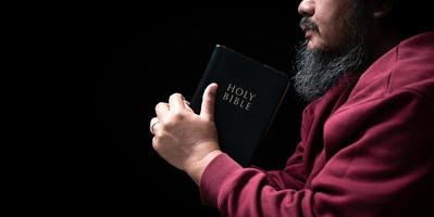 Hands folded in prayer on a Holy Bible in church concept for faith, spirituality and religion, man praying in morning. Man hand with Bible praying. Person Christian who faith in Jesus worship in dark. photo