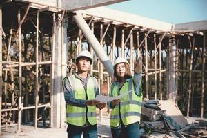 Two specialists inspect commercial, Industrial building construction site. Real estate project with civil engineer, designing commercial buildings on paper. Skyscraper concrete formwork frames. photo