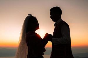 silueta de una pareja de novios enamorada cogida de la mano durante el amanecer con el fondo del cielo matutino. retratos antes de la boda. imágenes de pareja feliz hombre y mujer con fondo de naturaleza de cielo foto