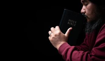 Hands folded in prayer on a Holy Bible in church concept for faith, spirituality and religion, man praying in morning. Man hand with Bible praying. Person Christian who faith in Jesus worship in dark. photo