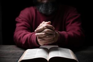 Hands folded in prayer on a Holy Bible in church concept for faith, spirituality and religion, man praying in morning. Man hand with Bible praying. Person Christian who faith in Jesus worship in dark. photo