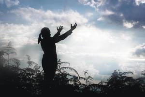 Christ religion and christianity worship or pray concept.Silhouette of Christian catholic woman are praying to god in dark sky. Prayer person hand in nature background. Girl believe and faith in jesus photo