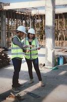 Two specialists inspect commercial, Industrial building construction site. Real estate project with civil engineer, designing commercial buildings on paper. Skyscraper concrete formwork frames. photo