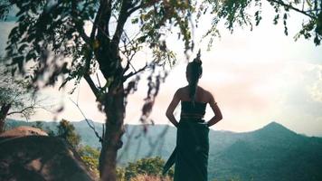 mujer asiática con un vestido largo y cabello negro parada frente al cañón para disfrutar de la vista desde la cima de la montaña video