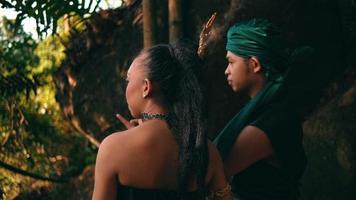 un asiatico coppia si blocca su insieme nel il foresta mentre indossare un' tradizionale verde vestito e parlando per ogni altro mentre godendo il Visualizza video