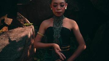 Asian woman in traditional green dress meditating lonely in peacefully in front of the big rock at the mountain video