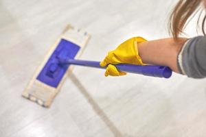 Girl in protective gloves cleaning floor using flat wet mop. photo