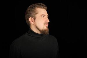 Cute bearded man, half-profile portrait, black background photo