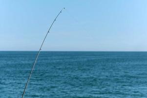 Fishing rod against blue ocean or sea background, copy space. Waiting for biggest haul. Meditative relax sport.