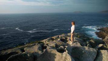 junge kaukasische frau, die auf dem felsen steht, während sie im meer schaut video