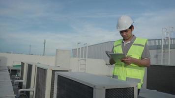 ingeniero de mantenimiento asiático trabaja en el techo de la fábrica. el contratista inspecciona el sistema de compresores y planifica la instalación de sistemas de aire acondicionado en la construcción. tecnología, verificación en línea. video