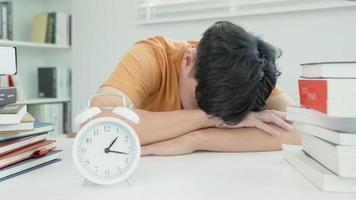 Asian student man turns off the alarm clock because he is tired from reading, male prepare for test and learning lessons in the library. stress, despair, haste, misunderstanding reading, discouraged. video