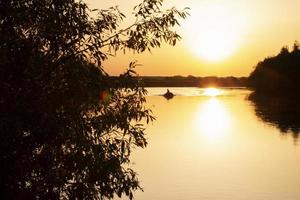 Sunset on the lake among the trees and in the distance a boat with a fisherman. photo