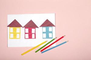Paper crafts for children. Application of children's creativity. Kindergarten and craft school. On a beige background, multi-colored houses made of colored paper.