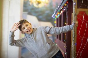 A happy little boy waves his hand from a toy wagon decorated with garlands. photo