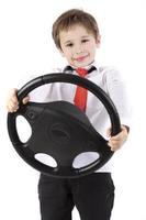 un niño gracioso sostiene el volante de un auto. joven conductor sobre un fondo blanco. foto