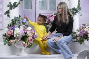 madre e hija multiétnicas están sentadas en el porche de la casa. alegre madre con pequeña hija de nacionalidad africana. familia de diferentes razas. foto