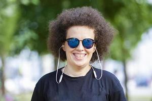 chica rizada con gafas de sol mira a la cámara y sonríe. foto