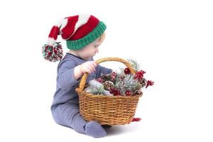 niño en un sombrero de navidad con una canasta de juguetes de navidad sobre un fondo blanco. foto